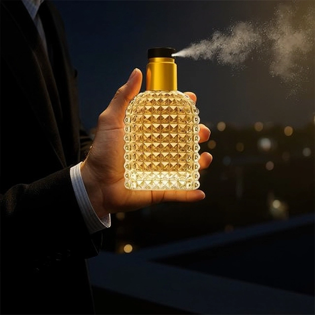 A man in a suit spraying a gold textured perfume bottle at night with a city skyline in the background